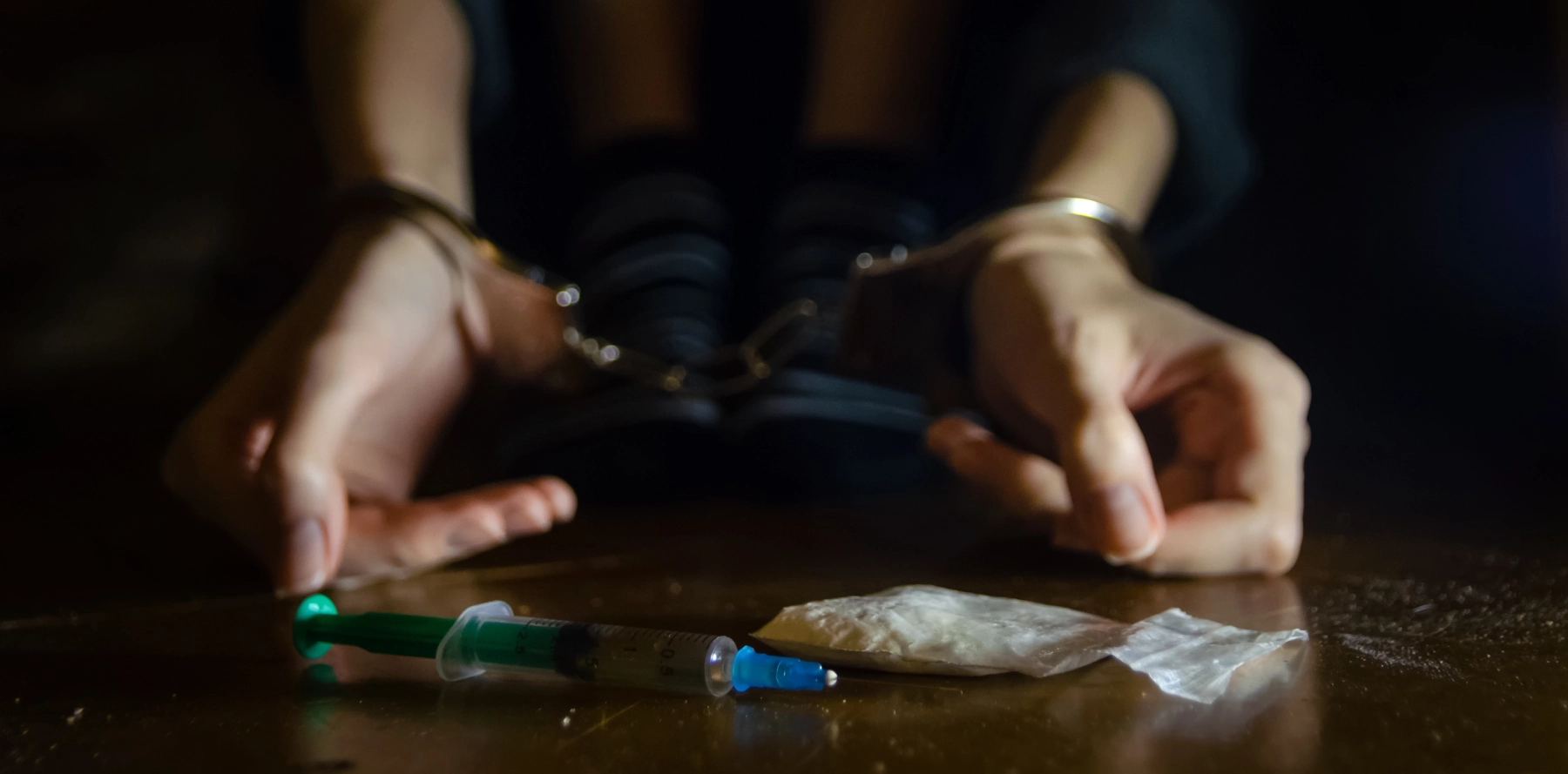 hands in handcuffs with multiple drugs in front