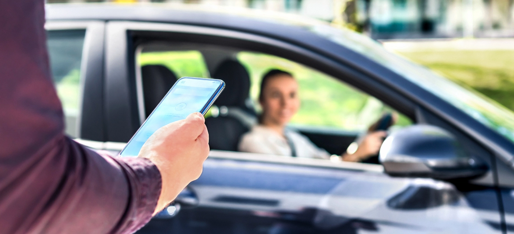 hand holding phone in front of a ride share vehicle